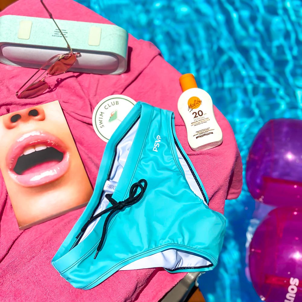PARADIS SVP blue swim Briefs lounging next to a pool woth sun protection, sunglasses, and inflatables. paradissvp.com