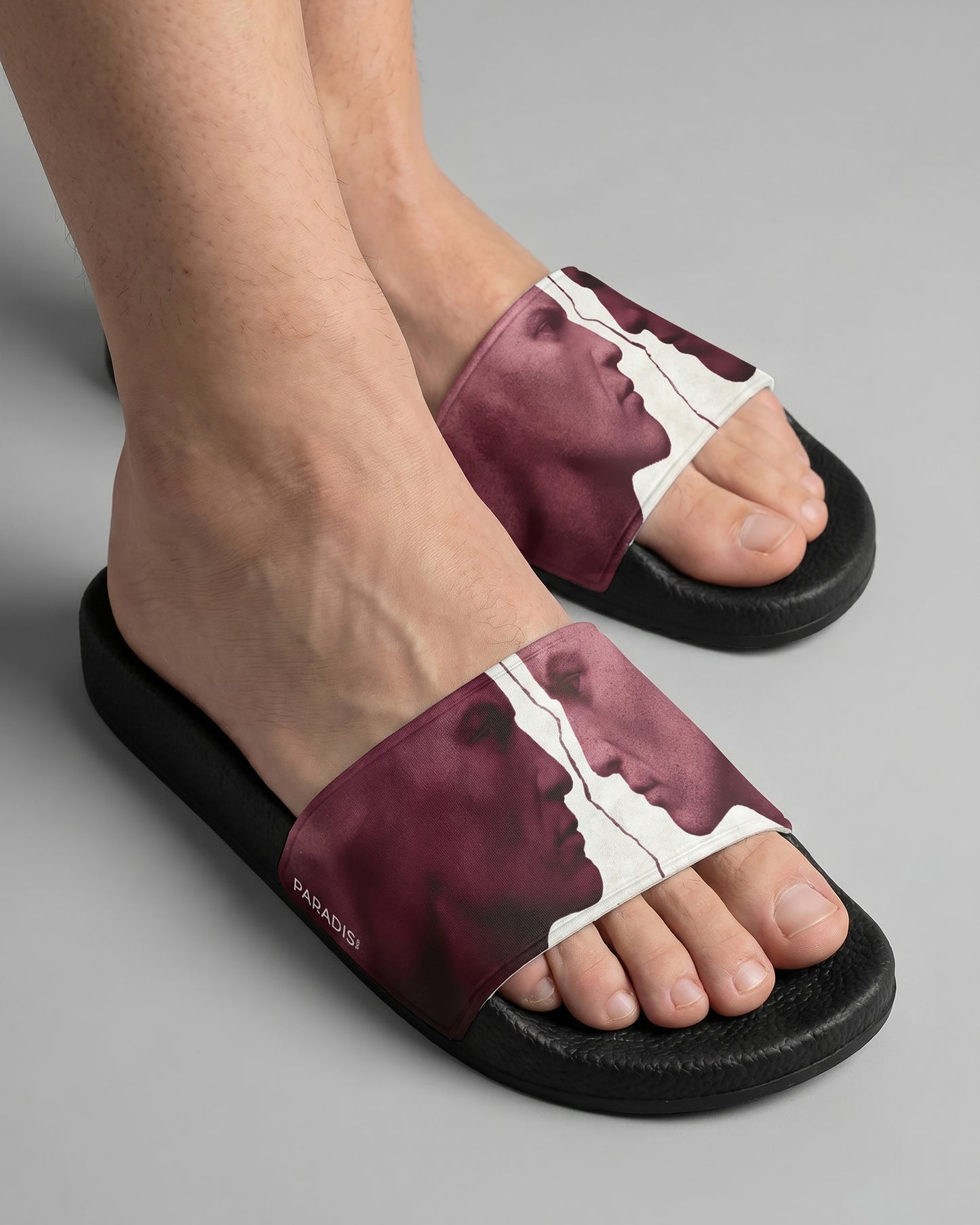 Model wearing a burgundy and white Pair of slides with artistic design of two statue faces on a white background