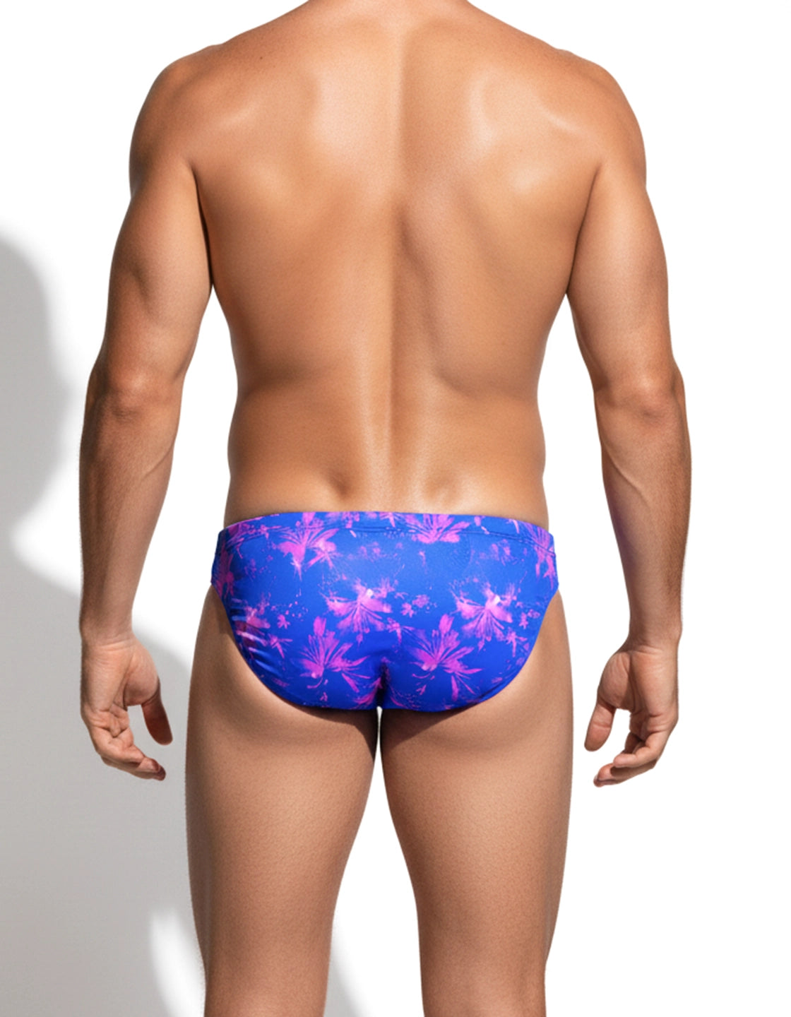 Back view of male model in a blue and pink floral pattern speedo-style swim brief on a white background by PARADIS SVP